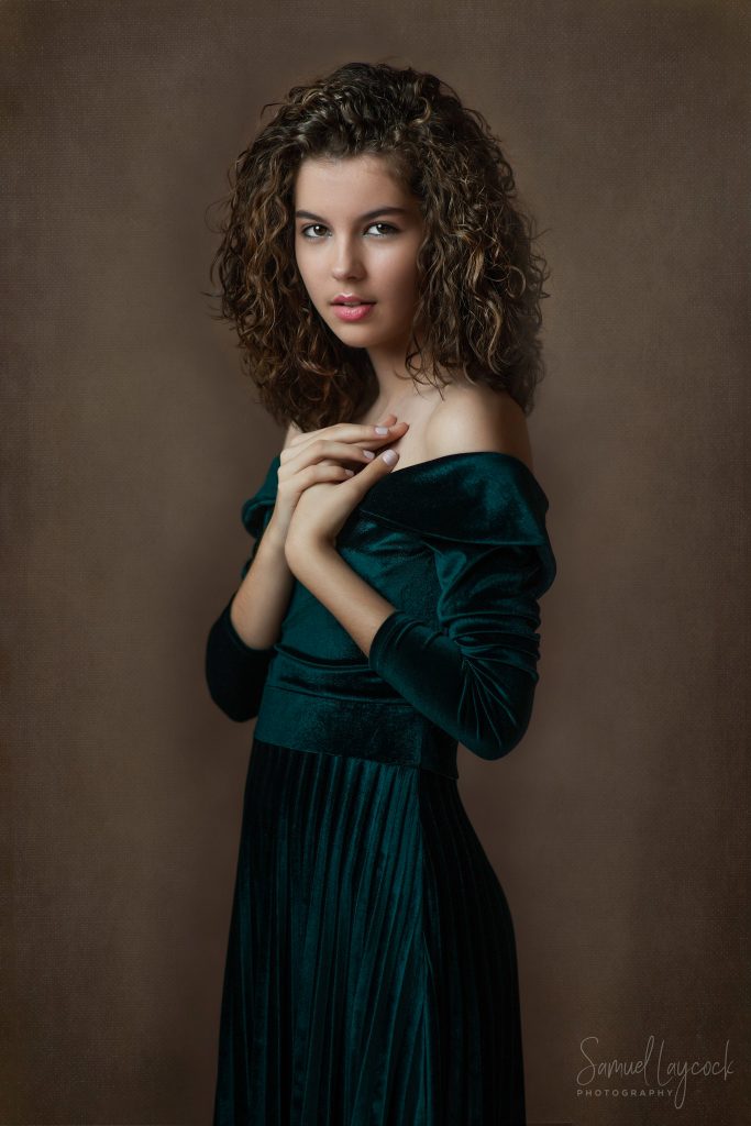 Young woman with her hands on her decolletage. Wearing a green velvet dress and with curly hair.