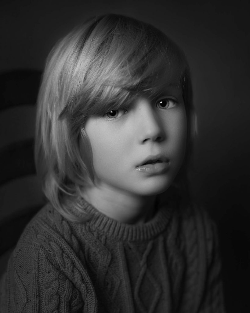 Young boy with slightly longer hair sat side on to the camera The picture is in black and white