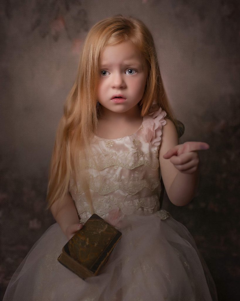 Young girl with her hair down holding onto a book and pointing into the camera