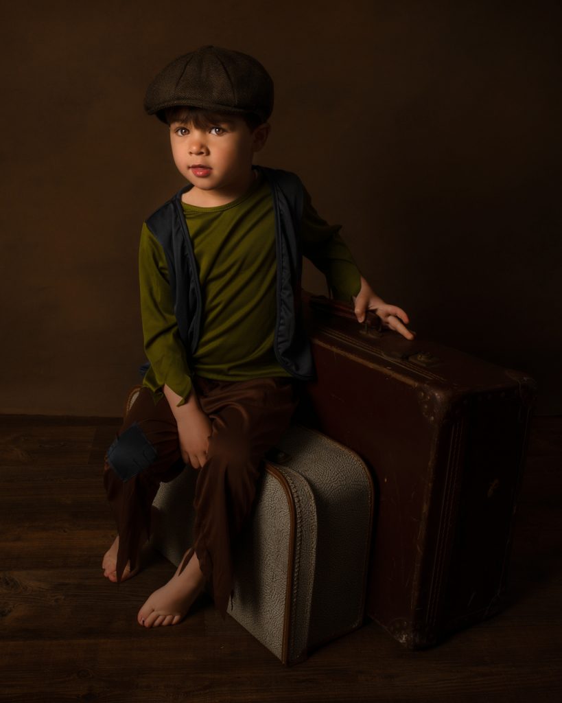 young boy in victorian dress sat on a vintage suitcase