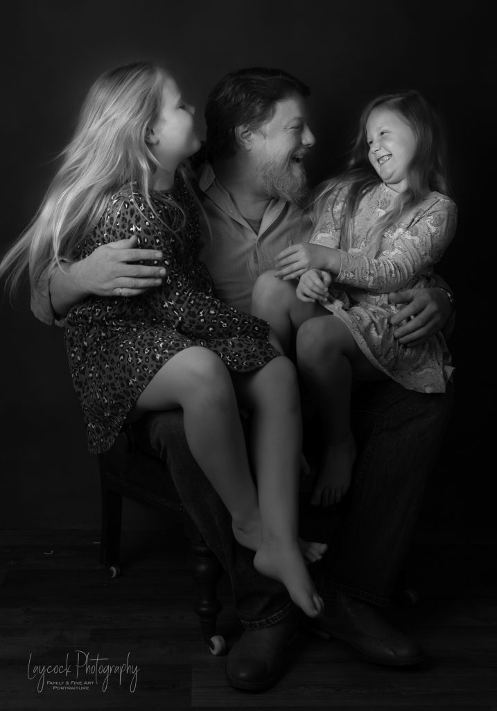 Dad with twin daughters on his knee in a black and white setting
