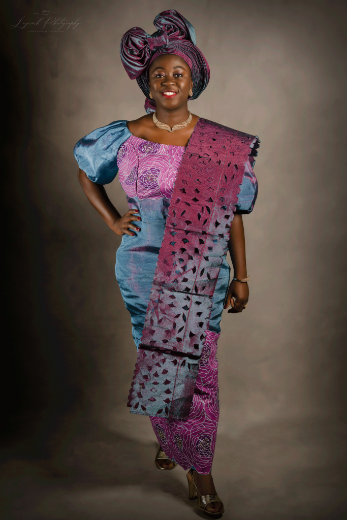 African woman wearing traditional dress. Stood upright with her right hand on her hip facing forward.
