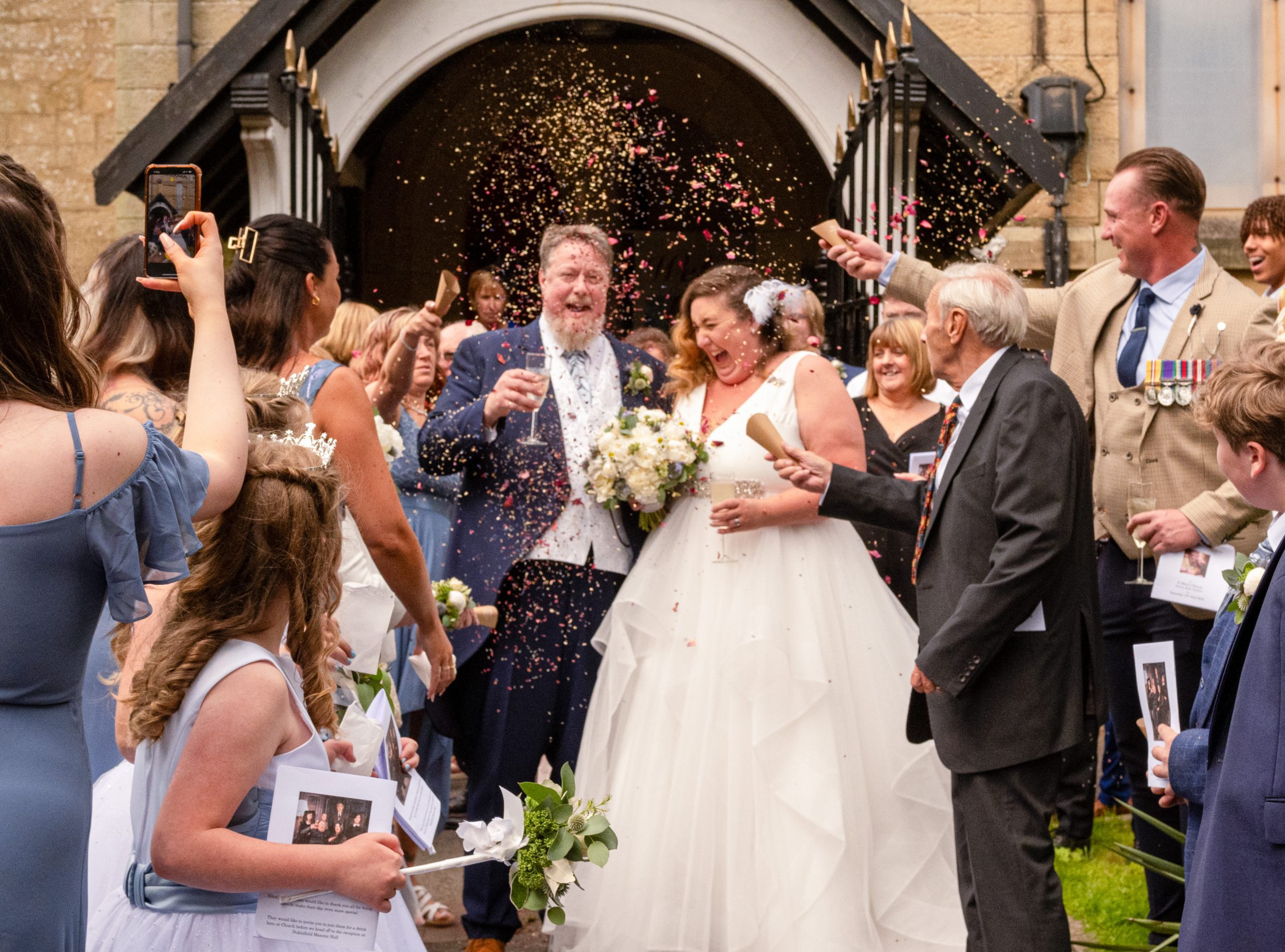 Bride and groom stood outside the church door, kissing whilst confetti is being thrown.